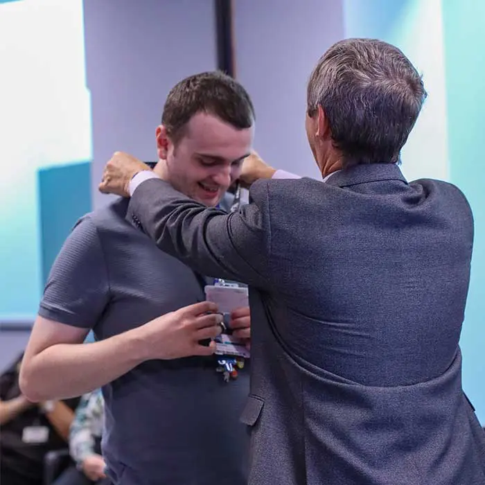 A man in a suit placing a medal around the neck of a smiling young man at an awards ceremony.