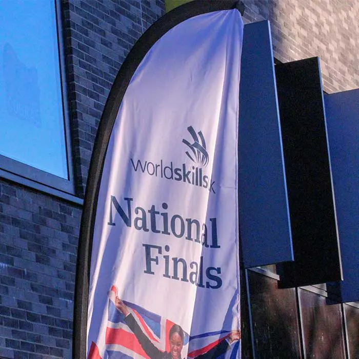 White feather banner outside a building featuring images of students. Text: 'WorldSkills National Finals'.